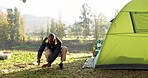 Camping, tent and black man setup in nature for shelter on outdoor holiday, vacation and adventure, Campsite, traveling and male person with hammer for pins for gear in woods, forest and countryside