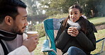 Couple, coffee and talking on camp chair outdoor in nature for fun, adventure and travel in woods. Man and woman or friends with drinks and conversation while camping for holiday, vacation or freedom