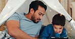 Bonding, tablet and father in a tent with kid watching a movie, video or show online. Happy, smile and young dad networking on social media with boy kid on digital technology in blanket fort at home.