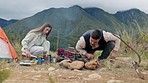 Talking, morning and a couple with a fire while camping in nature for a holiday, travel or trekking. Summer, conversation and a young man and woman making a bonfire with coffee in a field on vacation