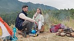 Couple, camping and fire with drinking water, outdoor and relax in mountains, nature or forrest for holiday. Man, woman and flames on ground for heat, cooking or vacation with chat, field and morning