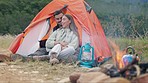 Couple, camping and fire in tent with hug, outdoor or relax together in woods, nature or forrest for holiday. Man, woman and bonfire on ground for heat, talking or vacation in bush, field and morning