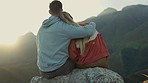 Hiking, view of mountain and happy couple hugging, relax on outdoor adventure and freedom in nature from back. Trekking, rock climbing and love, man and woman at sunset sky sitting on cliff together.