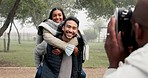 Couple, piggyback and photographer at park to take picture, bonding and smile on holiday in winter fog. Interracial, man and woman taking photo on vacation for happy memory, love and care in nature