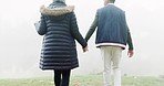 Couple, holding hands and walking in misty fog, travel or adventure together in the nature outdoors. Rear view of man and woman exploring natural environment in mist weather on holiday trip outside