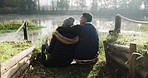 Hiking, hug and couple back by a lake in nature on vacation with camping and love. Outdoor, adventure and sitting with view in forest on a journey feeling peace on holiday in woods with young people