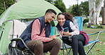 Couple, reading and cellphone at camp with happiness in nature for travel or conversation. Friends, together and technology camping trip in woods for adventure with social media or video for app.