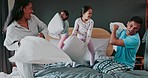 Energy, bedroom and kids in a pillow fight with their parents for fun, playful or bonding together. Happiness, smile and girl children playing with their mother and father on bed in their family home