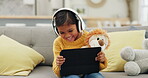 Tablet, headphones and happy girl or child learning, home education or listening to translation or education audio on sofa. Kid with teddy bear, games or watch funny comedy or cartoon on digital tech