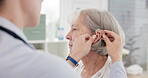Consultation, doctor and hearing aid for senior woman at clinic for help with ear problem. Hearing, treatment and installation with elderly female for listening with medical expert for solution.