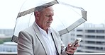 Senior, business man and phone with rain reading a text with a smile and umbrella. Winter, professional and mobile networking by a urban building with online web message and internet browse outdoor