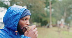 Hiking, morning and a black man drinking coffee in the rain while outdoor in nature to relax. Camping, winter and a young male tourist in the forest or woods for travel and freedom with a cup of tea