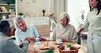 Senior people, friends and playing cards at a table while laughing and talking in nursing home. Elderly women, man and caretaker with tea and a game for bonding and to relax together in retirement