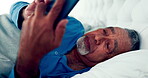 Phone, bed and a senior man reading a text message in the morning while in his home to relax during retirement. Mobile, social media and elderly male pensioner lying in the bedroom for communication