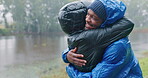 Camping, love and an interracial couple hugging in the rain while outdoor in nature together for romance or adventure. Smile, freedom or travel with a man and woman hiking in wet winter weather