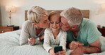 Phone, games and grandparents kissing a girl on a bed in the home for playing together or bonding. Love, kids or family with senior man and woman loving their granddaughter on a mobile in the bedroom