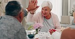 High five, poker and senior friends at a tea party together during a visit in a home for bonding. Smile, retirement and support with a group of elderly people in a living room for a social gathering