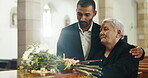 Funeral, church and senior mother and man mourning death by coffin with flowers. Grief, family and son with mom by casket to console, support or interracial empathy for depressed or sad elderly woman