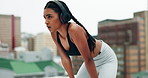 Woman, headphones and fitness on rooftop for break or rest after running exercise or workout in city. Tired female person breathing from intense cardio training, recovery or practice in an urban town