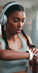 Fitness, headphone and a woman with a watch at gym for running, progress and time. Indian athlete person listening to music, podcast or audio on health app for exercise motivation, focus and wellness