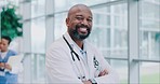 Crossed arms, smile and face of a man doctor standing in the medical hospital with confidence. Happy, professional and portrait of mature African male healthcare worker in hallway of medicare clinic.