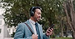 Headphones, phone and businessman walking outdoors listening to music, playlist or album. Technology, networking and professional male lawyer streaming song while browsing on his cellphone in a park.