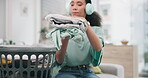 Laundry, headphone and woman packing clothes and cleaning in a home living room doing housework for hygiene. Sorting, music and young tidy person or cleaner working on household task in a lounge