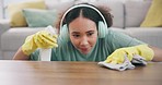 Housekeeping, headphones and woman wipe the table with detergent, cloth and gloves at home. Female maid, cleaner or housewife listening to music, playlist or radio while cleaning furniture for dust.