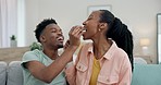 Black couple on sofa, feeding popcorn and love on date night together in living room in home. Relax, African man and happy woman eating snacks on couch with romance, fun and romance in apartment.