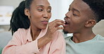 Couple, love and feeding snacks on home sofa while bonding, happy and romantic in a lounge. Black man and woman eating and relax on a couch in a healthy relationship with care, happiness and trust