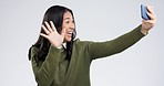 Smile, wave and a woman on a video call with a phone for communication on a white background. Happy, meeting and a girl speaking on a mobile and blowing kiss while live streaming on a studio backdrop