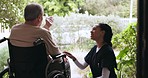 Nurse, talking and man in a wheelchair in garden to relax with caregiver, conversation and nature in retirement home. Elderly, patient and worker in healthcare chat with person with a disability 