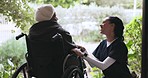 Caregiver, talking and woman in a wheelchair in garden to relax with nurse, conversation and nature in retirement home. Elderly, patient and worker in healthcare chat with person with a disability