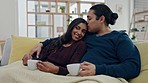 Love, coffee and couple watching a film on sofa in the living room for relaxing together. Kiss, happy and young man and woman with smile drinking cappuccino and streaming show, movie or video at home