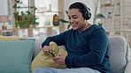 Smile, sofa and a man with a phone and headphones for music, online chat and happy with an app. Relax, home and a young person streaming or listening to audio or a sound from a mobile on the couch