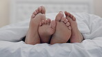 Feet, couple and rubbing in bedroom in home, relax in peace or rest in blanket in the morning together. Barefoot, bed and man and woman sleeping in comfort, bonding to play and care for love in house