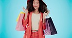 Fashion, shopping bag and dance with face of woman in studio for boutique, retail and wardrobe. Product, choice and luxury with portrait of customer on blue background for promotion, gift and sales