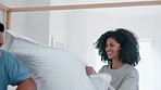 Happy couple, bed and playing pillow fight in fun morning, wake up or bonding together at home. Interracial man and woman smile in happiness for weekend, holiday or break with cushion in bedroom