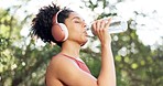 Woman, fitness and drinking water in headphones, sports  and cardio training, running exercise or workout in nature. African person or tired runner listening to music and liquid bottle for nutrition
