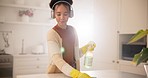 Woman in headphones in kitchen cleaning with gloves, spray bottle and smile, working and listening to streaming radio. Music, housework and happy housewife with chores to wipe dust or dirt in home.