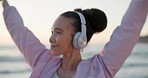 Dancing, headphones and young woman at the beach for an outdoor cardio workout or training. Happy, energy and female person moving and listening to music, playlist or radio by the ocean for exercise.