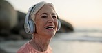 Happy, headphones and senior woman at the beach for outdoor cardio workout or training. Smile, fitness and elderly female person listening to music, playlist or radio by ocean for exercise at sunset.