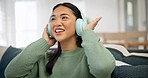 Headphones, smile and woman dance on a sofa in the living room listening to music, playlist or radio. Happy, singing and young Asian female person streaming a song or album for relaxing in apartment.