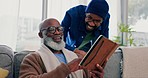 Discussion, notebook and man with his senior father on sofa in living room for journaling together. Happy, conversation and young African male person talking to his elderly dad for planning in lounge