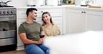 Happy couple on floor in kitchen with wine, cheers and smile to celebrate love, marriage and new home. Toast with alcohol in glass, man and woman, relax drink and conversation in apartment together.