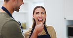 Couple, apron and feeding fruit in home kitchen for romance, healthy marriage and nutrition. A happy man and woman cooking and eating a strawberry with love for diet, taste or vegan food in a house