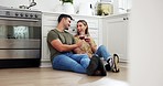 Happy couple on floor in kitchen with red wine, cheers and smile to celebrate love, marriage and happy home. Toast with alcohol, man and woman on ground to relax in conversation in apartment together