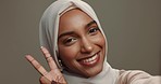Selfie, smile and Islamic woman with peace sign, beauty and social media on a grey studio background. Face, Muslim person or model with v gesture, symbol or support with fashion, makeup or motivation