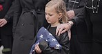 Funeral, cemetery and girl with American flag for veteran for respect, ceremony and memorial service. Family, depression and sad child by coffin in graveyard mourning military, army and soldier hero