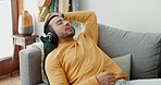 Music, headphones and asian man relax on a sofa with audio, streaming or track in his home. Earphones, radio and male with wellness app in a living room with podcast for resting, nap or day off peace